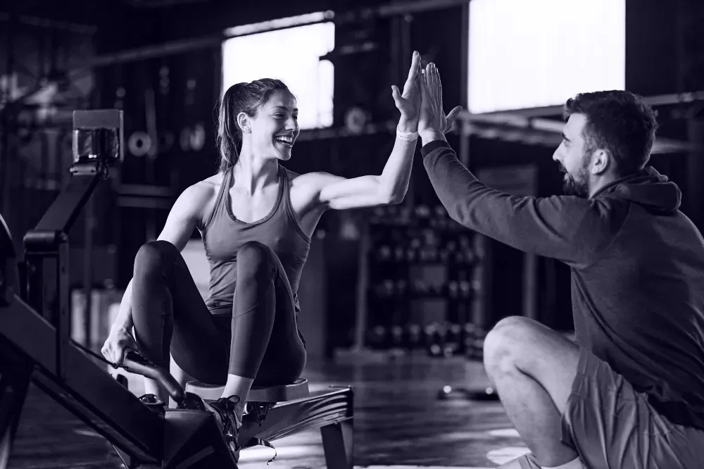 Femme sur rameur avec coach, high-five